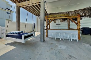 A beach house with a swing bed, a thatched roof bar, and a white outdoor seating area. - Tiki Pool Club (Galveston)