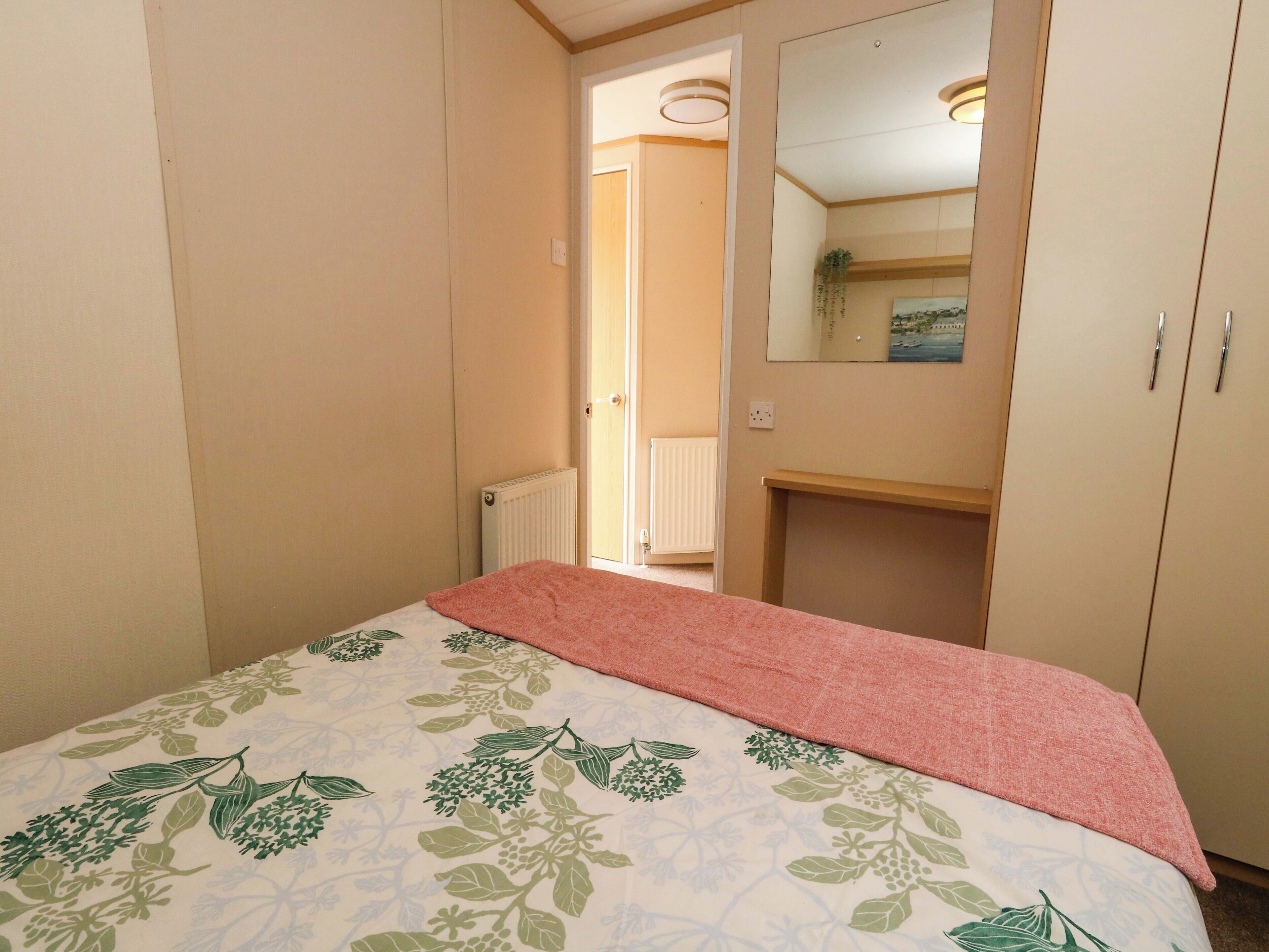 A bedroom with a bed, a mirror, a radiator, and a door leading to another room.