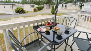 A balcony with a table set for dining, chairs, and a view of mobile homes in the background. - Foxglove 4 (Ringwood)