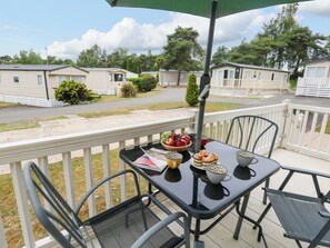Un balcón con mesa lista para comer, sillas y vista a casas móviles al fondo.