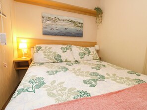 Una habitación de hotel con una cama, una mesita de noche con lámpara, un cuadro en la pared y una planta en el alféizar de la ventana.