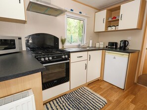 A compact kitchen with a stove, oven, microwave, sink, and a small refrigerator. - Foxglove 4 (Ringwood)
