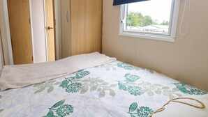 A bedroom with a bed, a window with a blue blind, and a view of buildings outside. - Foxglove 4 (Ringwood)