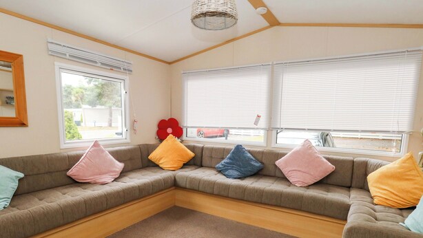 A corner living room with a sectional sofa, a woven ceiling light fixture, and large windows with blinds. - Foxglove 4 (Ringwood)