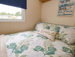 A bedroom with a bed, a pillow with 'home' embroidered, a wall decoration with an anchor and text, and a window with blinds. - Foxglove 4 (Ringwood)