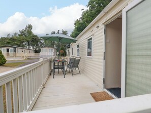 Una casa móvil con un patio amueblado con mesa, sillas y una sombrilla, además de una puerta corrediza.