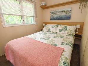 Ein Schlafzimmer mit einem Bett, einem Fenster mit Jalousien, einem Bild an der Wand und einem Nachttisch mit Lampe.