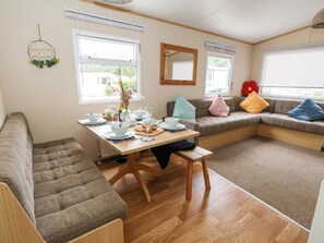 A cozy living area with a sofa, a dining table set with plates, glasses, and a vase of flowers. - Foxglove 4 (Ringwood)