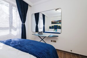 A bedroom with a bed, an ironing board, a mirror, and a painting on the wall. - Luxurious Breakaway in Nairobi, Kilimani surrounded by all amenities. (Nairobi)