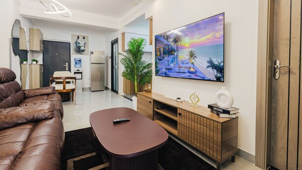 Una sala de estar moderna con un sofá de cuero, una mesa de centro de madera, un televisor y un cuadro grande con una playa.