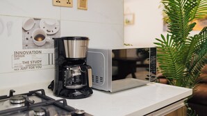 Una cocina con cafetera, microondas y una pared decorada con una taza de café y una cuchara.