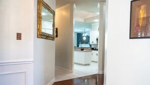 A hallway leading to a kitchen with white cabinets and a wooden floor. - Executive 4BR Retreat Mins to AT&T Stadium (Arlington)