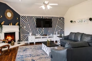 Ein Wohnzimmer mit Kamin, Wand mit Schwarz-Weiß-Muster, Flachbildfernseher, schwarzes Ledersofa und Couchtisch.