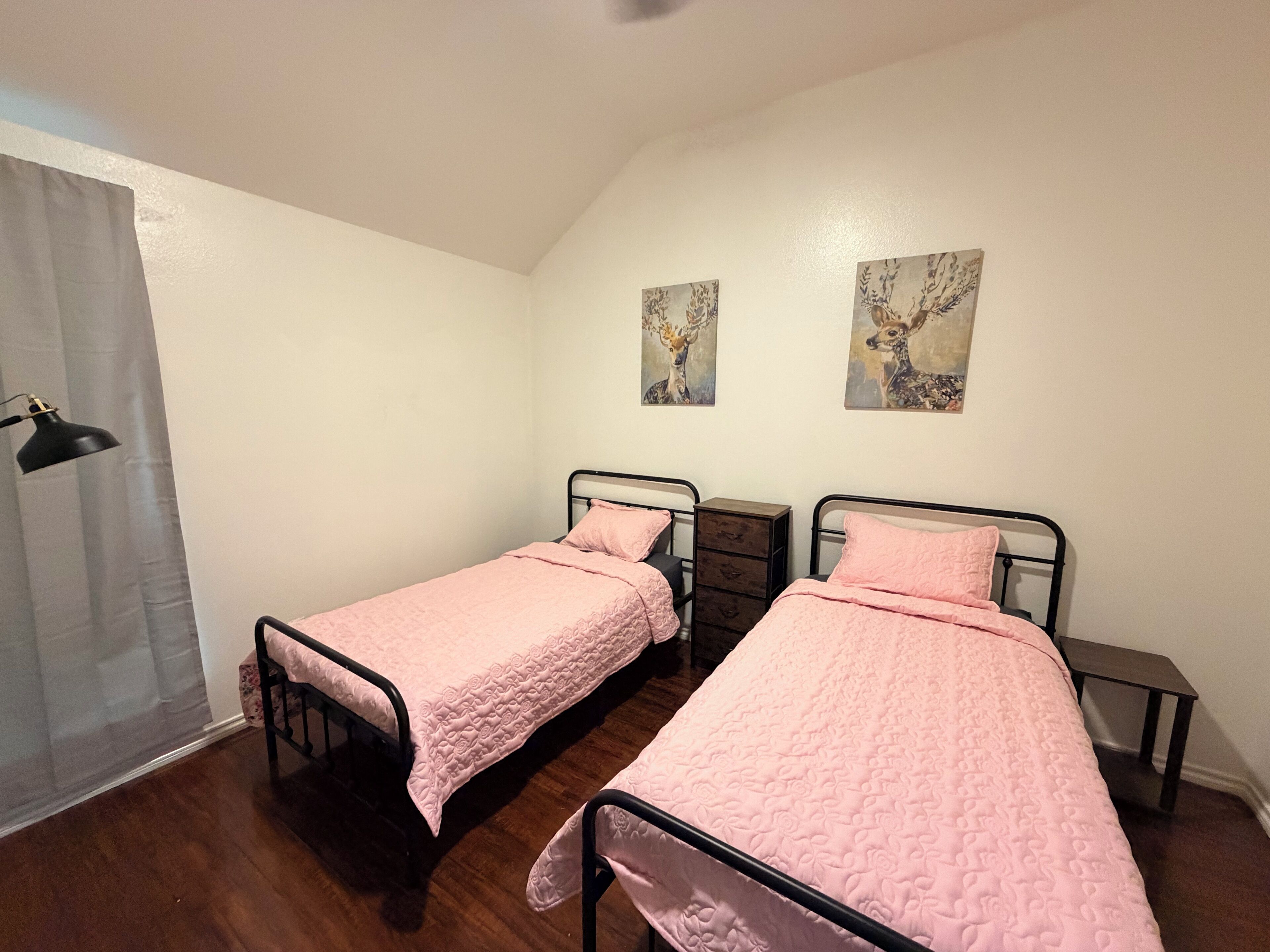 A bedroom with two single beds, a nightstand, a lamp, and two wall art pieces.