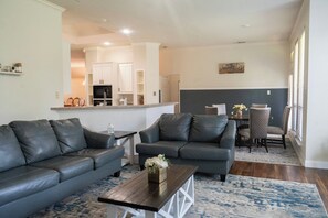 Ein Wohnzimmer mit zwei grauen Sofas, einem Couchtisch und einem Essbereich mit Tisch und Stühlen.