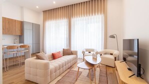 Un salon moderne avec un canapé, des fauteuils, une petite table et un téléviseur.