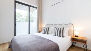 A modern hotel room with a large bed, a wooden nightstand, a lamp, and a sliding glass door leading to an outdoor area. - ASTRO Emanuelle E by LovelyStay (Leça da Palmeira)