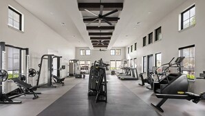 Ein geräumiger Fitnessraum mit unterschiedlichen Trainingsgeräten, großen Fenstern und einer hohen Decke.