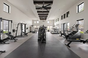 Ein geräumiger Fitnessraum mit unterschiedlichen Trainingsgeräten, großen Fenstern und einer hohen Decke.