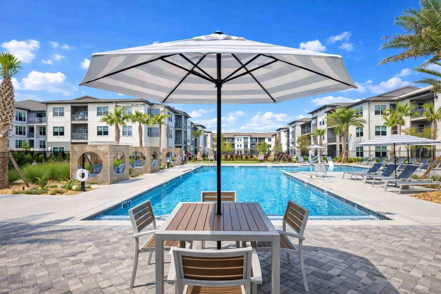 A swimming pool with lounge chairs and a table, surrounded by apartment buildings.
