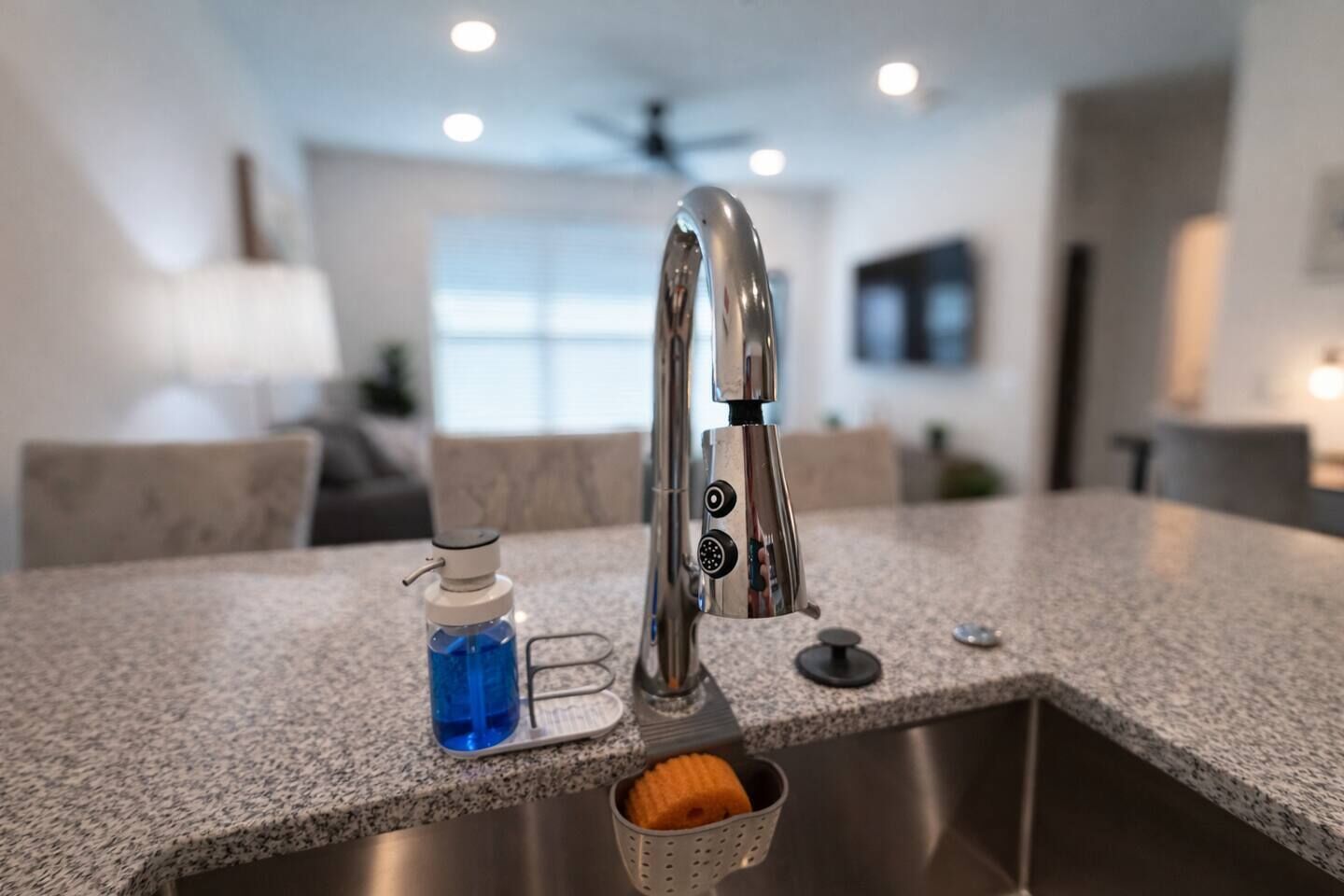 A kitchen with a stainless steel faucet, a soap dispenser, and a sponge holder.