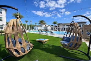 A pool area with hanging chairs, a pool, and a lawn.