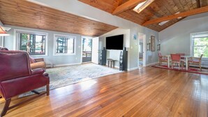 A spacious living room with wooden floors, a red leather sofa, a flat-screen TV, and a dining area with chairs and a table.