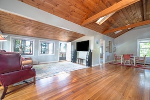 A spacious living room with wooden floors, a red leather sofa, a flat-screen TV, and a dining area with chairs and a table.