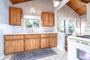 A kitchen with wooden cabinets, a white countertop, a hanging light fixture, and a stove.