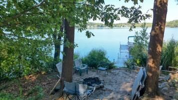 Un terrain de camping au bord du lac, équipé d’un foyer, de chaises et d’une jetée qui s’avance dans l’eau.