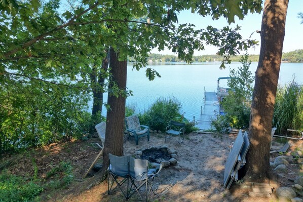 Un camping junto al lago con un pozo de fuego, sillas y un muelle que se adentra en el agua.