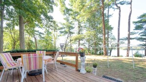 A wooden deck with outdoor furniture, a pergola, and a view of a lake surrounded by trees.