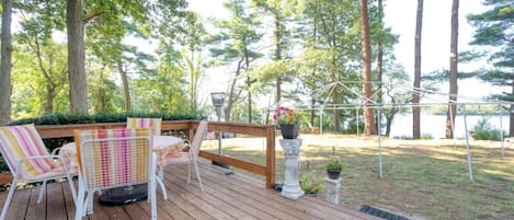 A wooden deck with outdoor furniture, a pergola, and a view of a lake surrounded by trees.