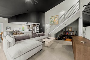 Ein modernes Wohnzimmer mit einem Ecksofa, einem Couchtisch, einer Treppe und einer Küchenzeile.