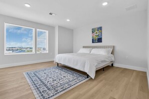 Une chambre Ă coucher avec un lit, une fenĂȘtre, un tableau et un tapis Ă motifs.