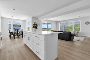 A spacious living area with a large island, a dining table, and a view of the outside.