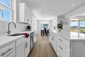 Una cocina moderna con muebles blancos, un lavamanos de acero inoxidable y una zona de comedor con vista al mar.