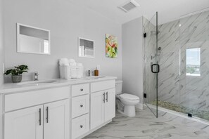 Un baño moderno con ducha de mármol, muebles de tocador blancos y una planta en maceta.