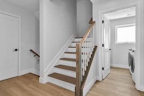 A staircase with wooden steps and white railings, a door with a black handle, and a laundry area with a washing machine.
