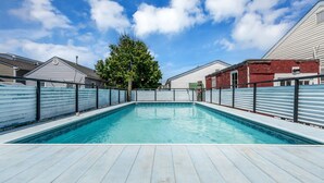 Ein Schwimmbecken mit Holzterrasse, umgeben von Metallzäunen, mit Häusern im Hintergrund.