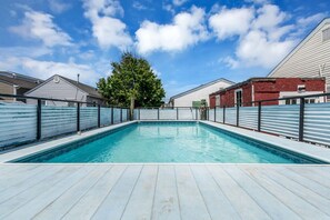 A swimming pool with a wooden deck, surrounded by metal fences, with houses in the background. - Private Pool, 3BR Jersey Shore Oasis (Seaside Heights)