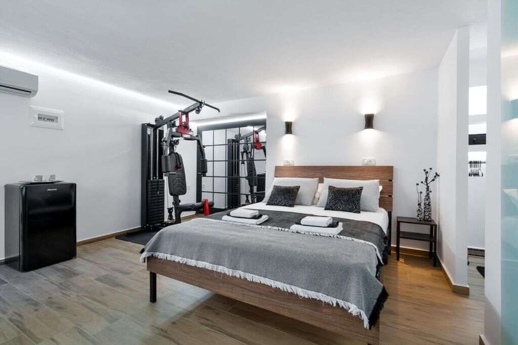 A modern bedroom with a bed, workout equipment, a small desk, and a wall-mounted air conditioner.