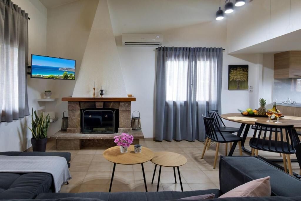 Un soggiorno moderno con camino, televisione, zona pranzo con sedie e cucina sullo sfondo.