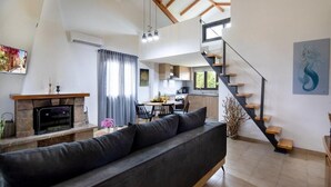 A modern living room with a sofa, fireplace, dining area, kitchen, and a staircase. - Santy Villa - Gerani (Gerani)