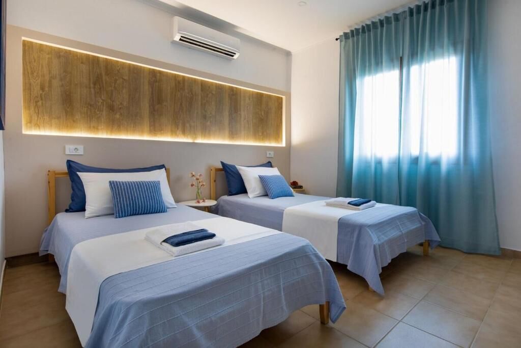 Une chambre d’hôtel avec deux lits, un mur recouvert de panneaux en bois, un climatiseur et une fenêtre avec des rideaux bleus.