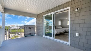A balcony with a view of the street, a sliding glass door leading to a bedroom with a bed and a window, and a gated area with a sign.