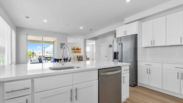 A modern kitchen with white cabinetry, a stainless steel refrigerator, and a dishwasher.