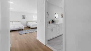 A modern bedroom with two beds, a white wardrobe, a bathroom with a mirror, and a wooden floor.