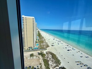 Blick auf einen Strand mit einem hohen Hotelgebäude, blauem Himmel und einem Sandstrand mit Sonnenschirmen.