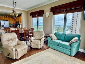 Ein Wohnzimmer mit einer Couch, Sesseln, einem Esstisch und einer Küche im Hintergrund.